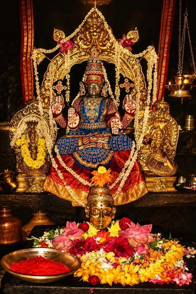 Goddess Sri Mookambika Devi of Kollur, seated in the sanctum with abhaya and varada hastas, adorned in blue and gold silk with jasmine garlands and lit lamps